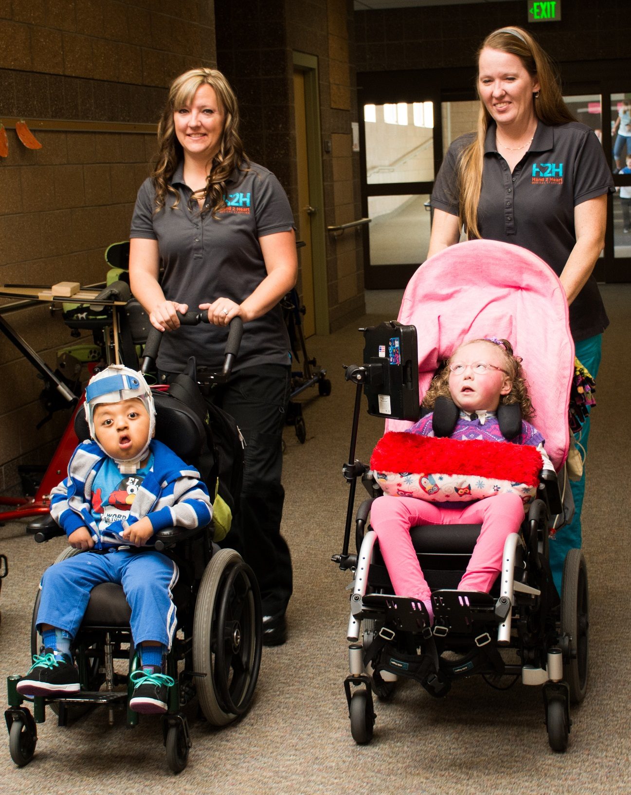 H2H nurses walking students in wheelchairs down a school hallway